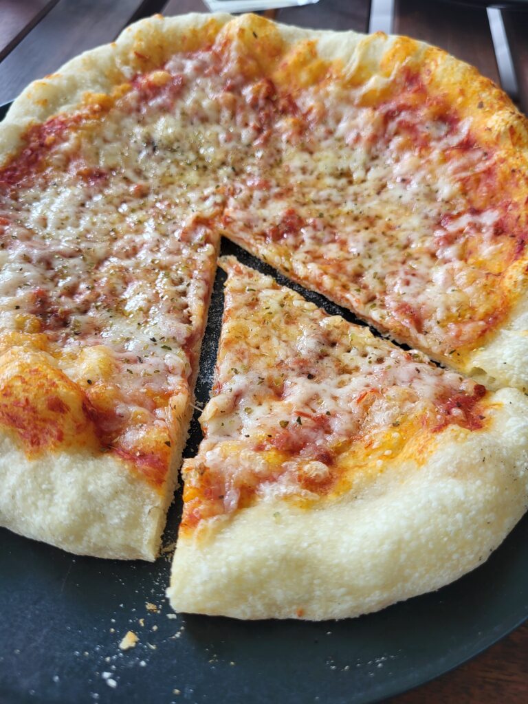 Eine Pizza Margherita. Ein Stück ist rausgeschnitten, man sieht den dünnen Boden. 